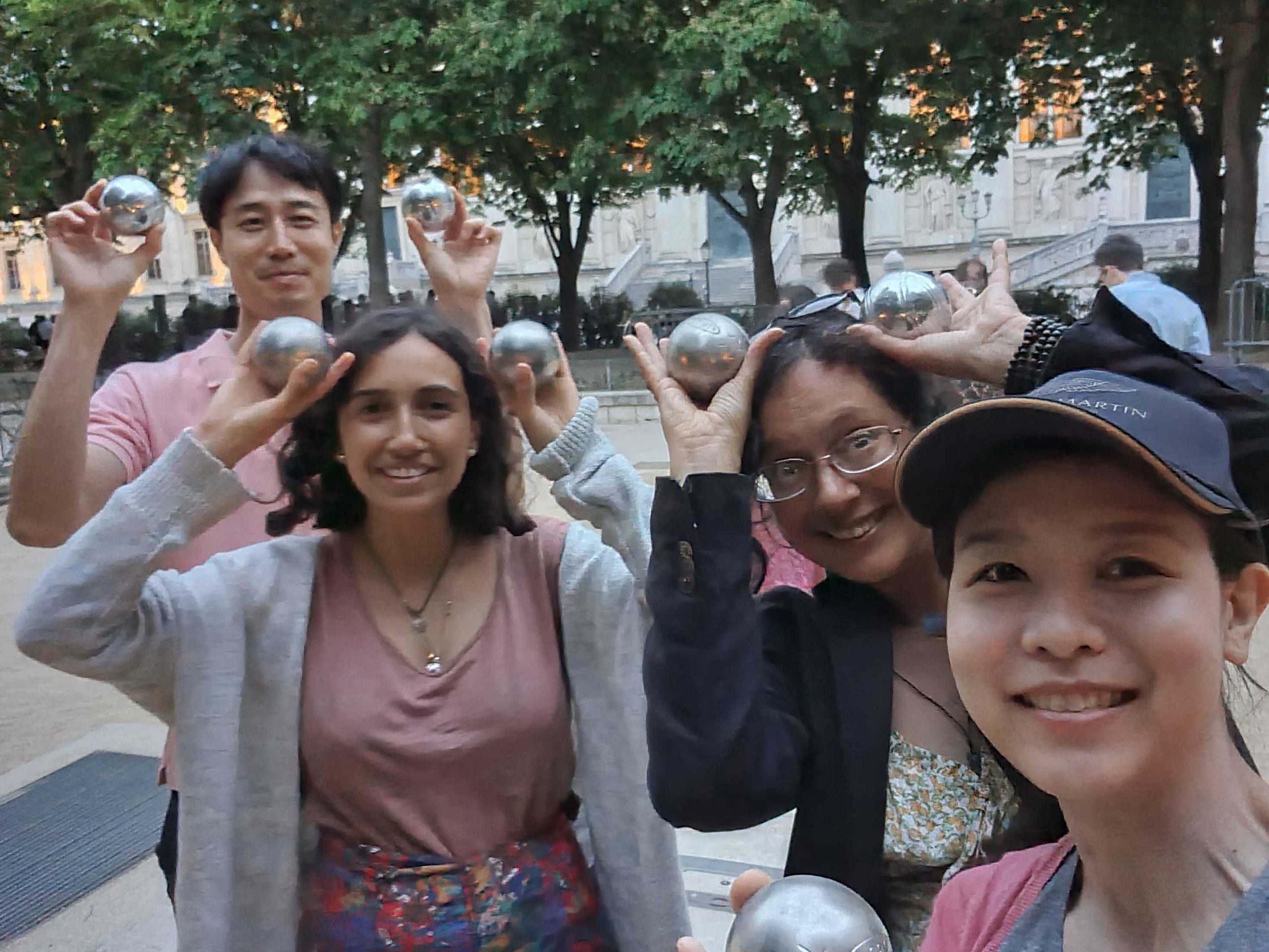 Happy expats holding pétanque balls during a kid-friendly pétanque evening in Paris, sharing laughter and cultural connection.